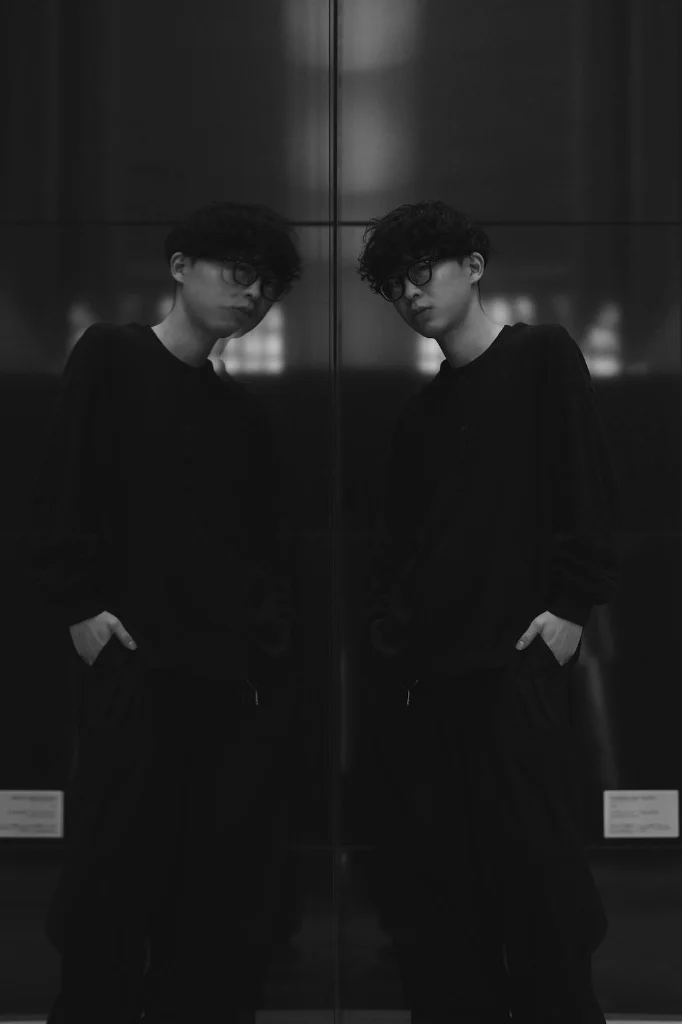 Yuki Hamaguchi のポートレート。ガラスに映った自分と向かい合っている
